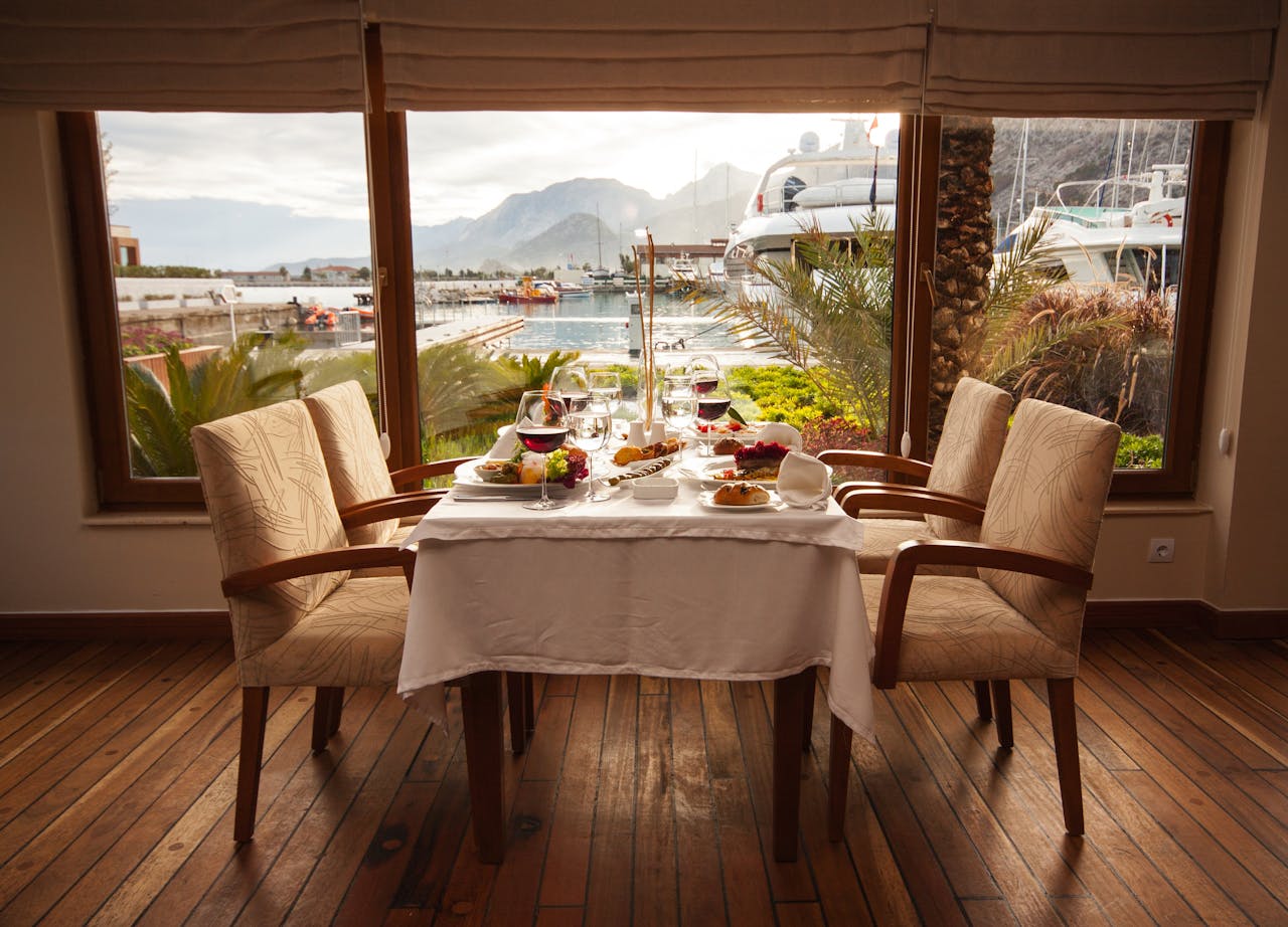 Elegantly set table in a seaside restaurant with a marina view, featuring gourmet dishes and fine dining setup.